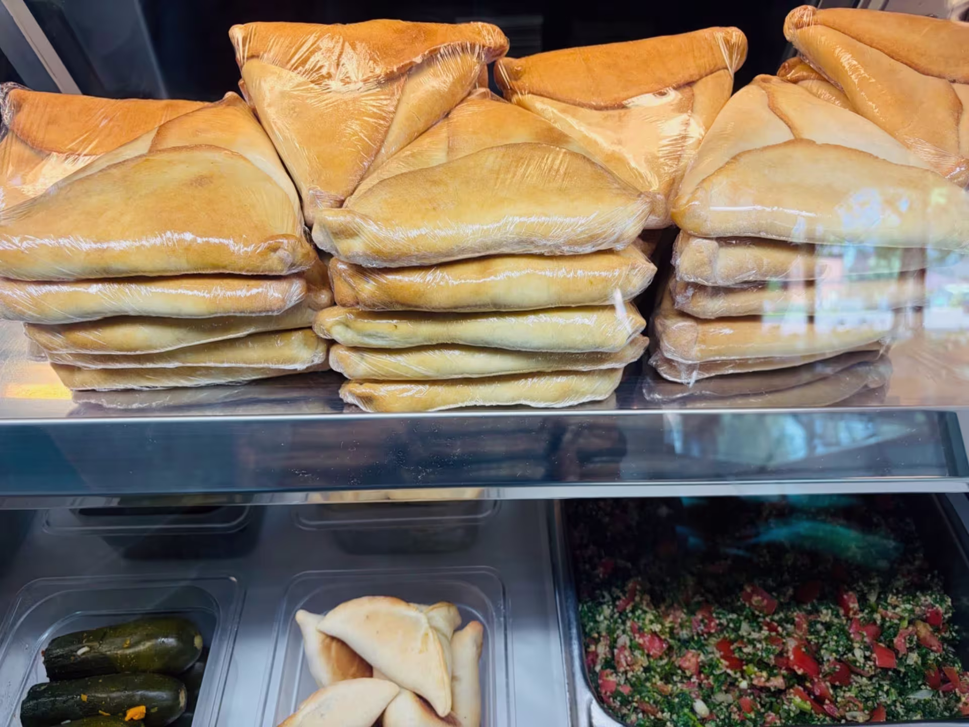 Various foods displayed in a deli case, in trays on two shelves