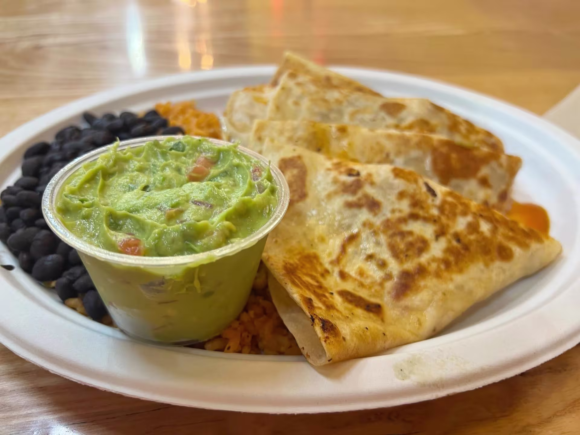 Close-up photo of guacamole, quesadilla, and black beans on white plate sitting on table