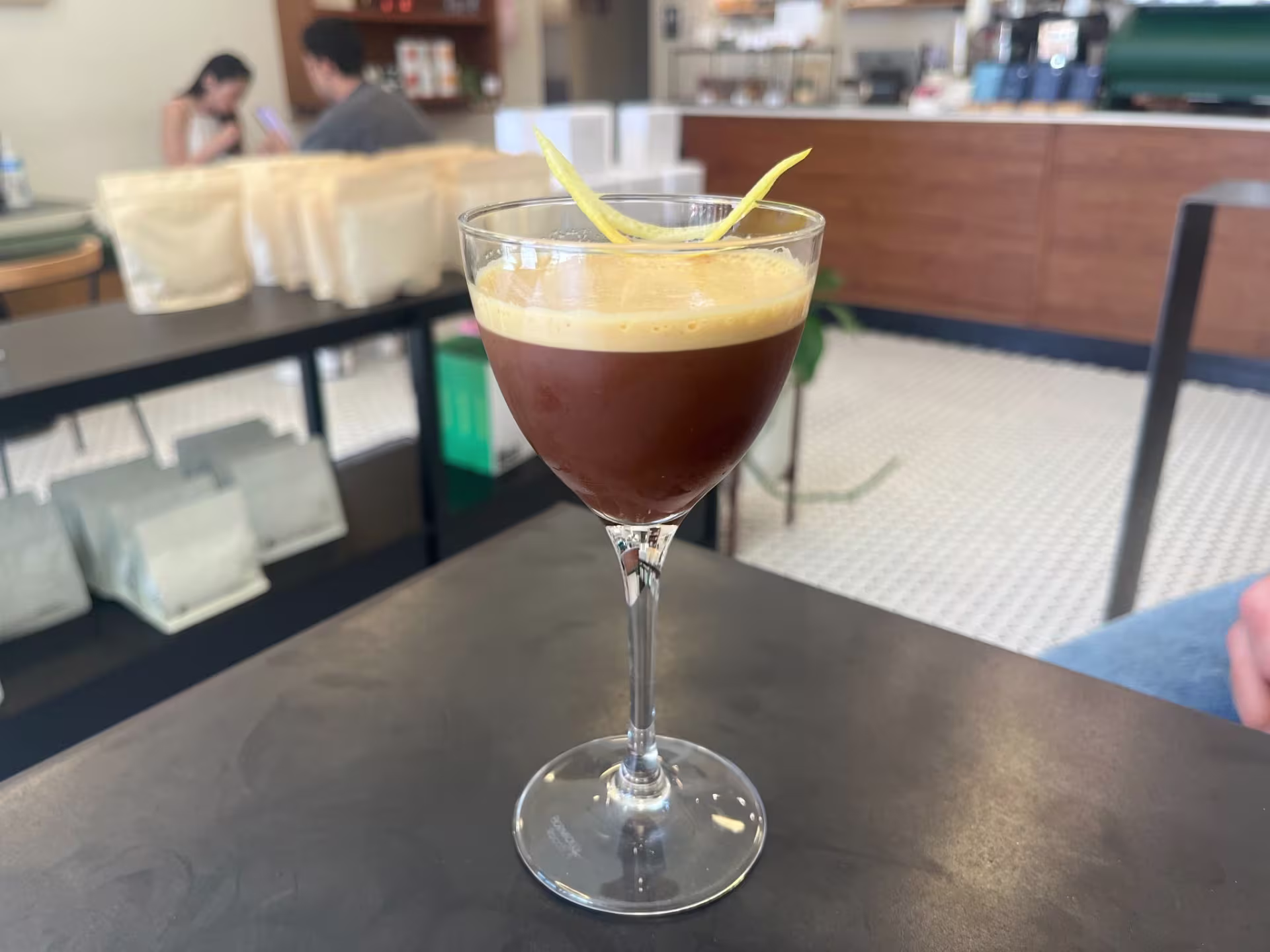 A wine glass containing a coffee with a thin layer of foam. Resting on the foam is a thin lemona peel