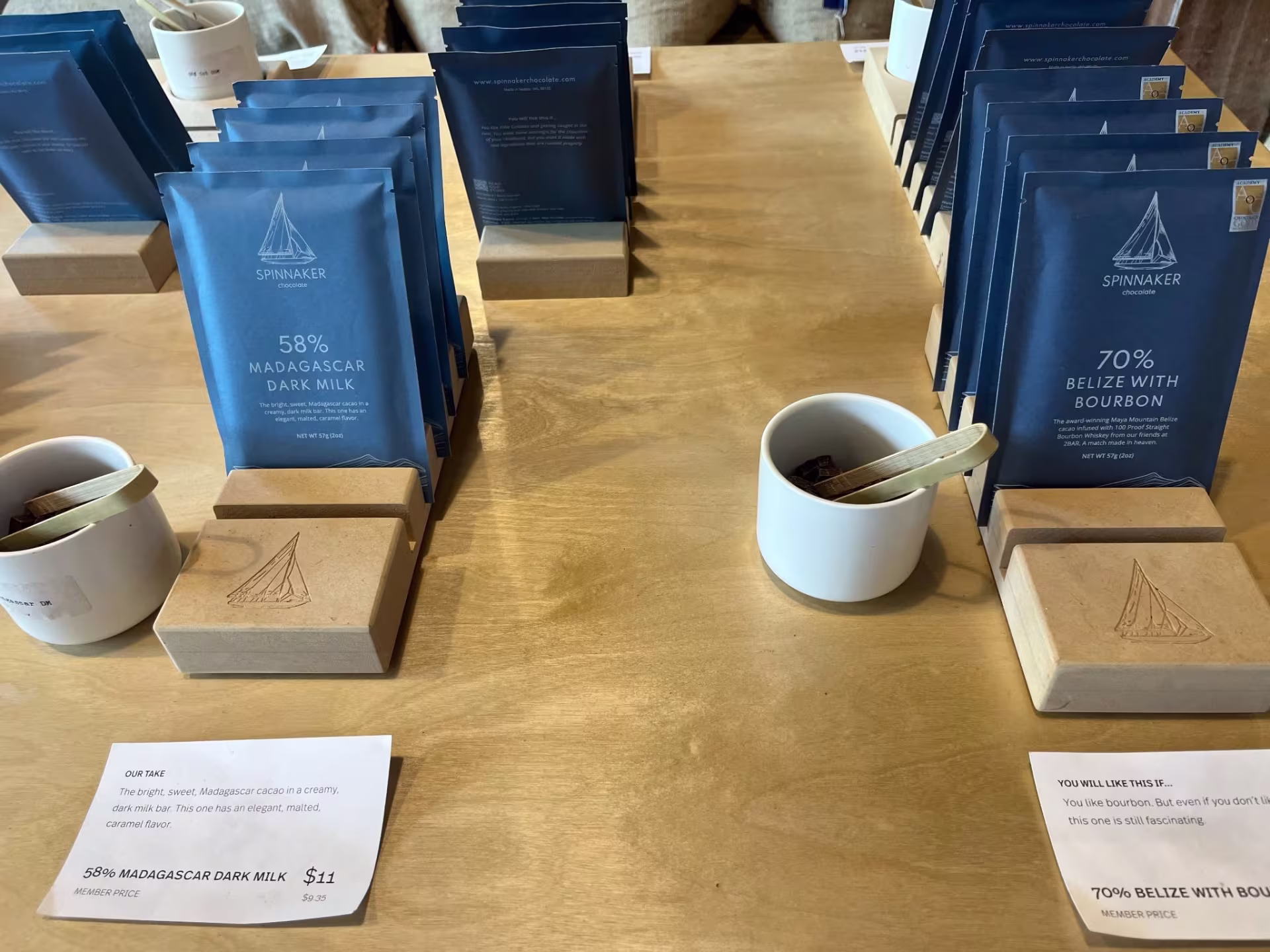 An arrangement of chocolate packages with samples in front. The left package says "58% Madagascar Dark Milk" The right package says "70% Belize With Bourbon"