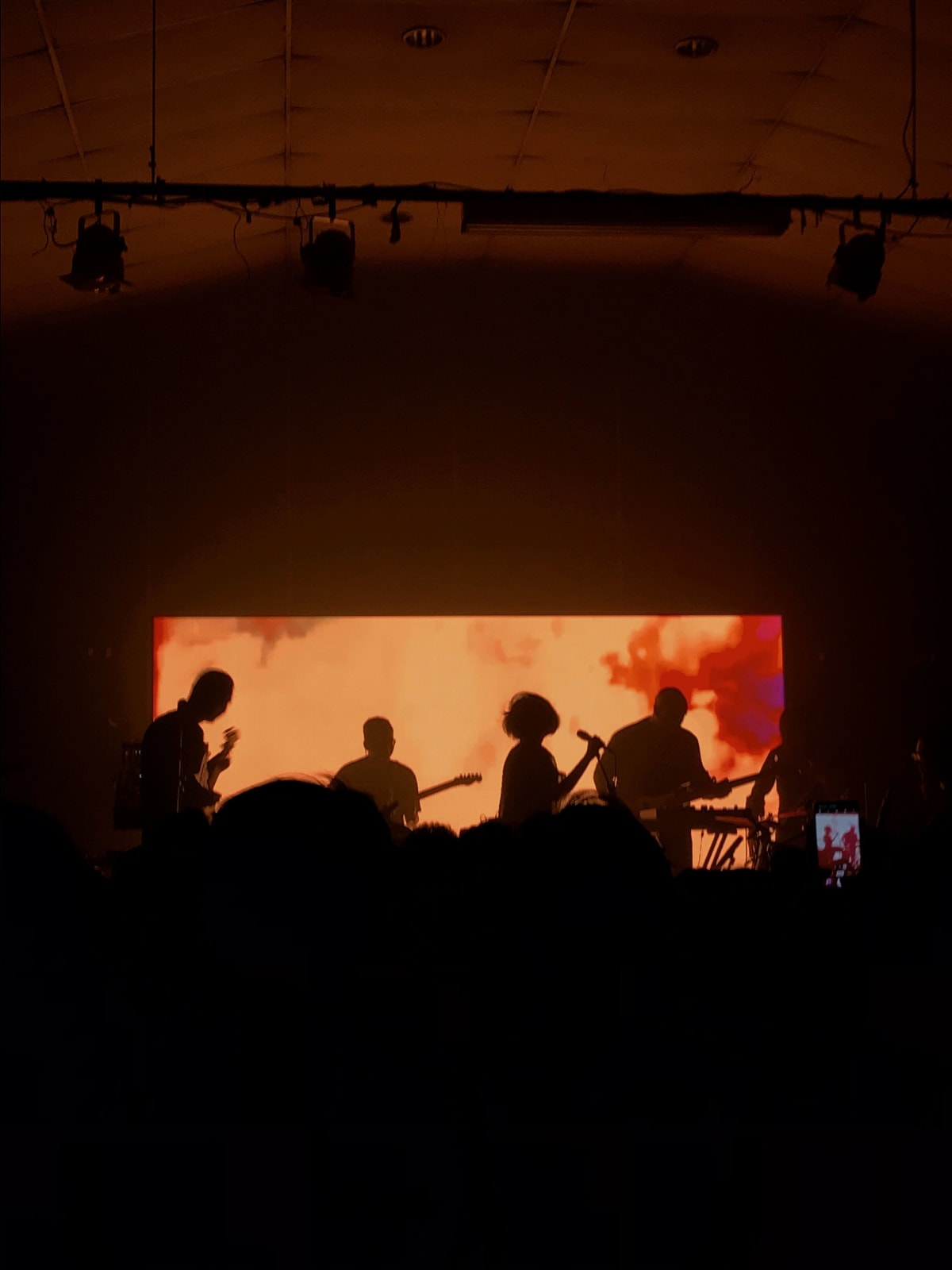 Pertunjukan Trees and the Wild dengan siluet band di bawah cahaya jingga dramatis