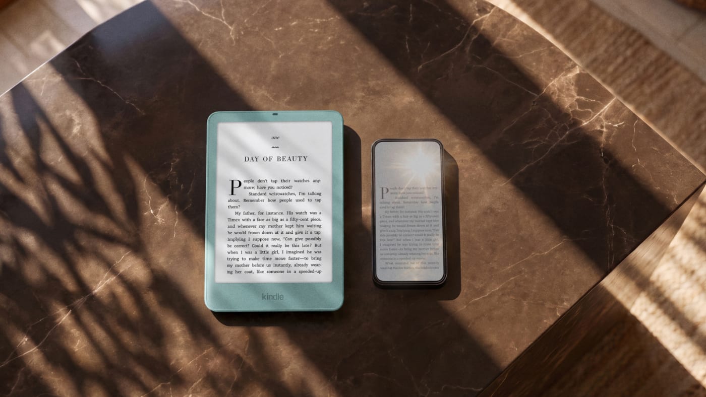 O novo Kindle básico, de moldura verde-água e tela nivelada com a borda, ao lado de um celular sobre uma mesa de mármore