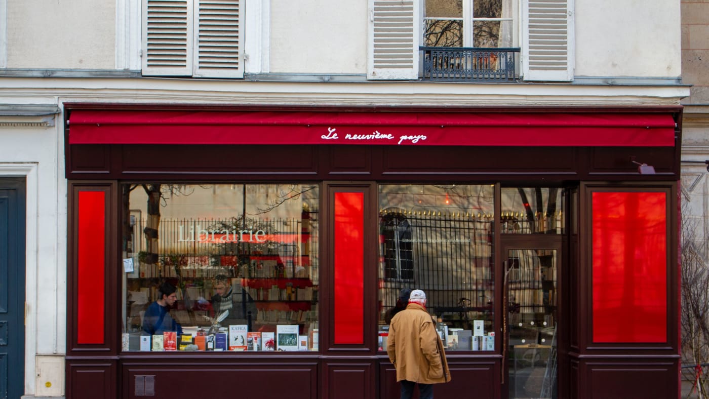 Homem olha a vitrine de uma livraria de fachada vermelha em Paris