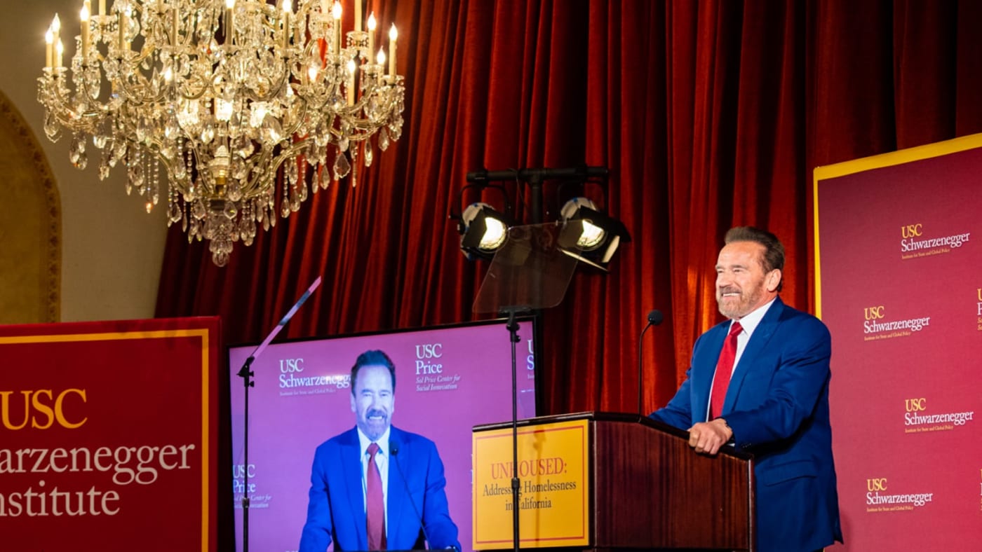 Arnold Schwarzenegger discursa em púlpito durante evento.