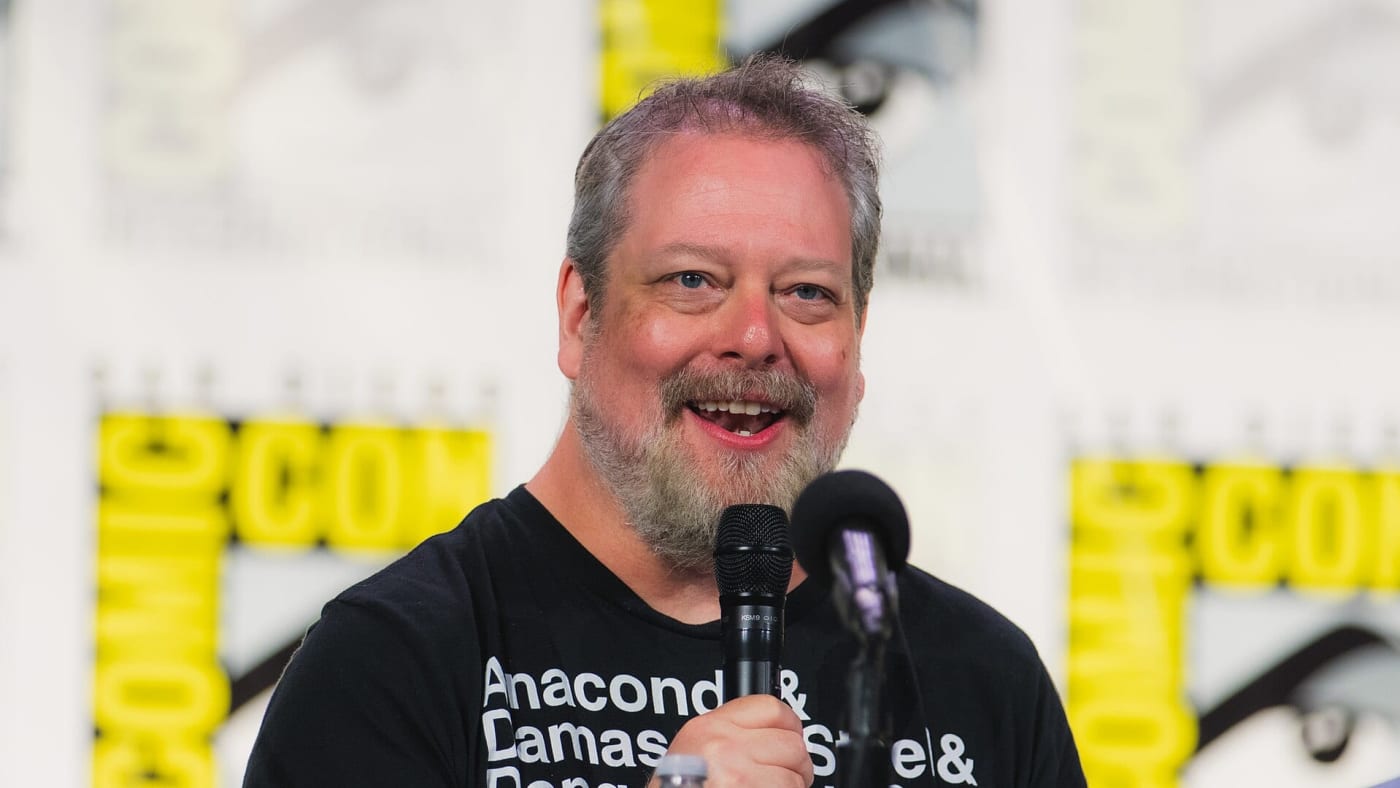 Matt Dinniman sorri e segura um microfone durante evento na Comic-Con.