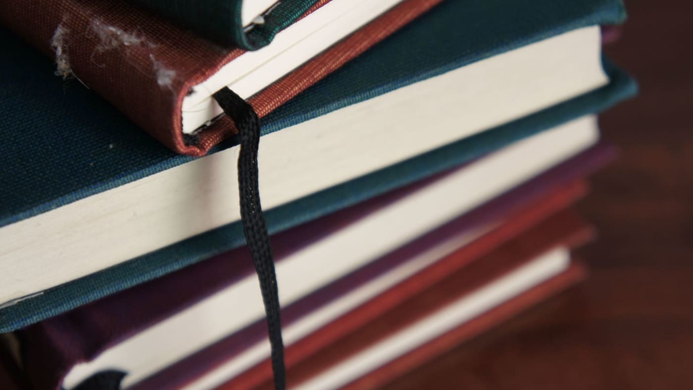 Pilha de livros de capa dura com fitas marcadoras em detalhe.