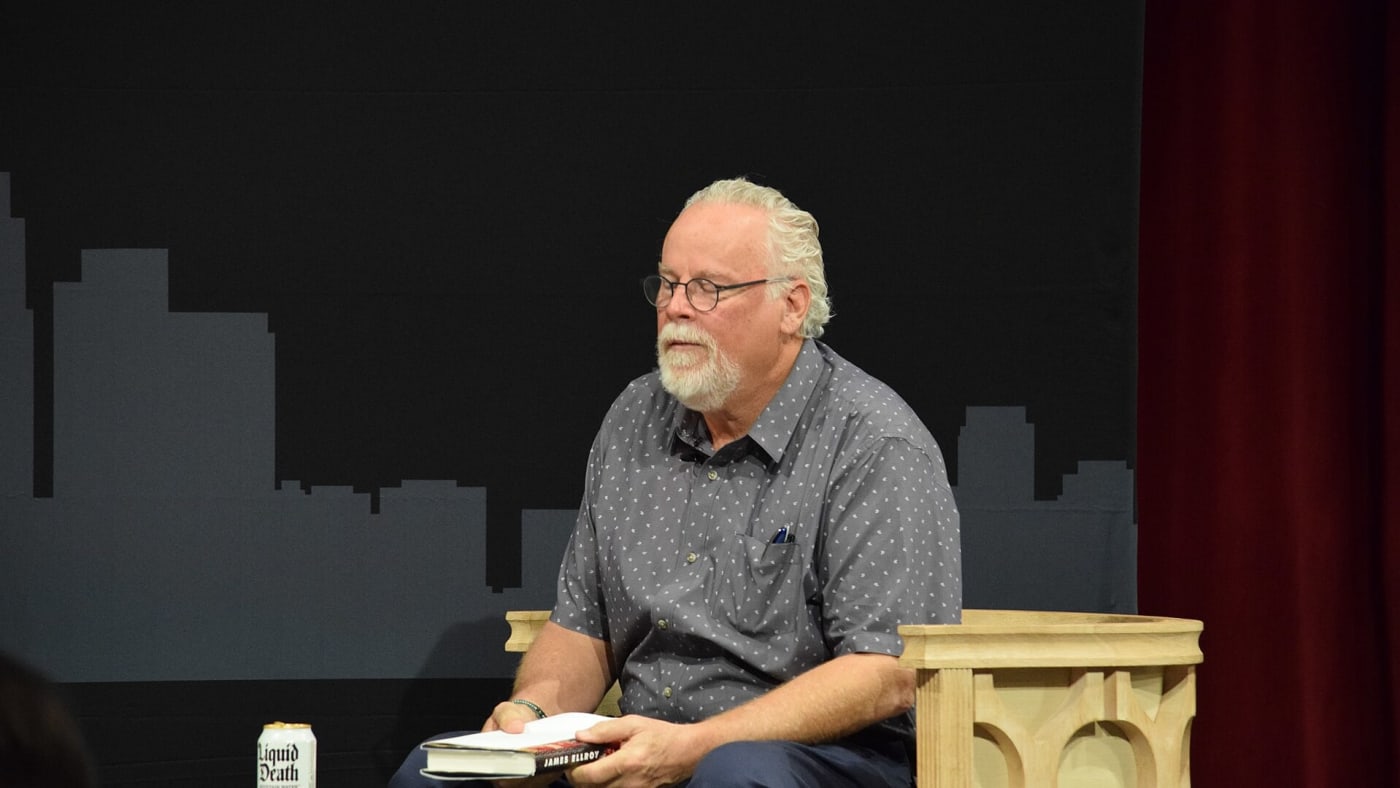 Michael Connelly sentado em um palco segurando um livro