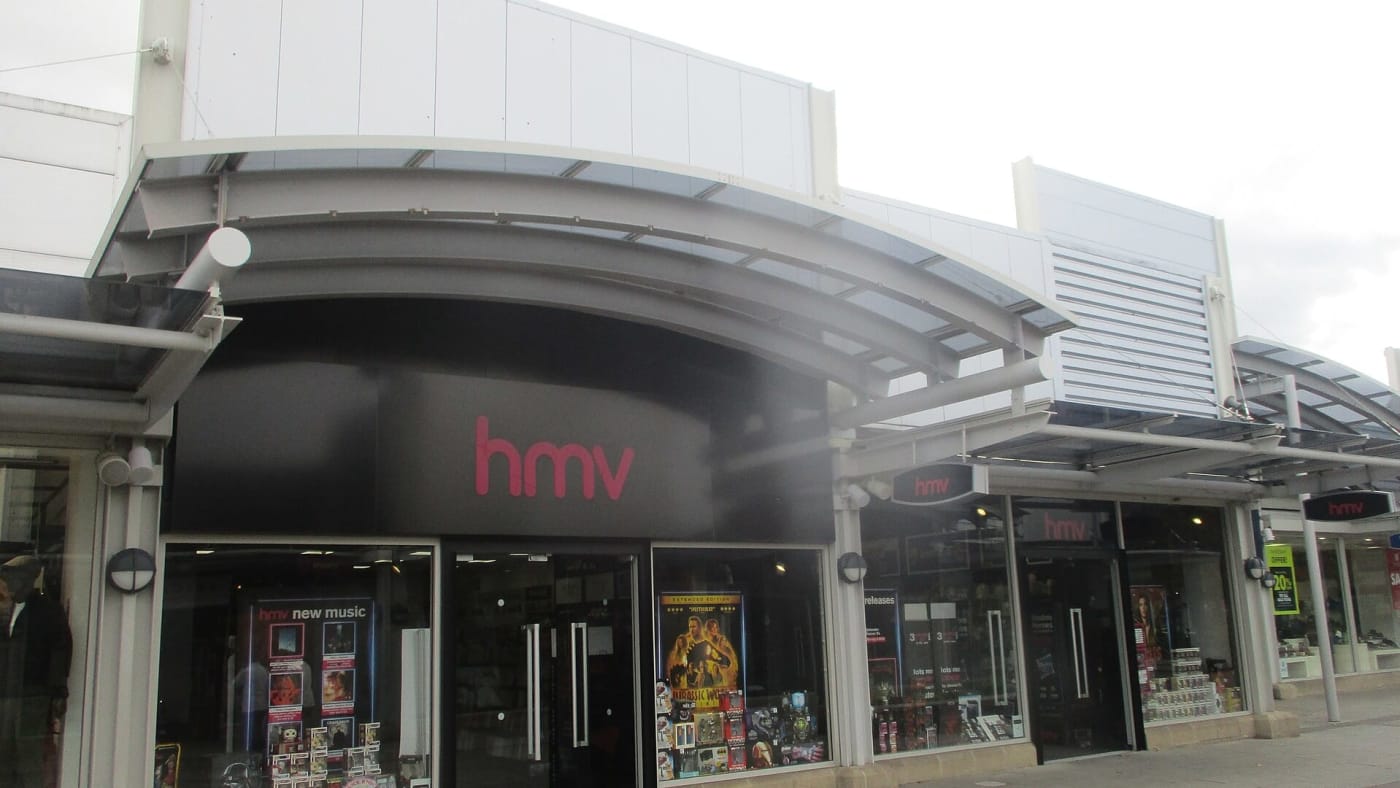 Fachada de uma loja da rede HMV com vitrines exibindo produtos e logotipo em destaque.