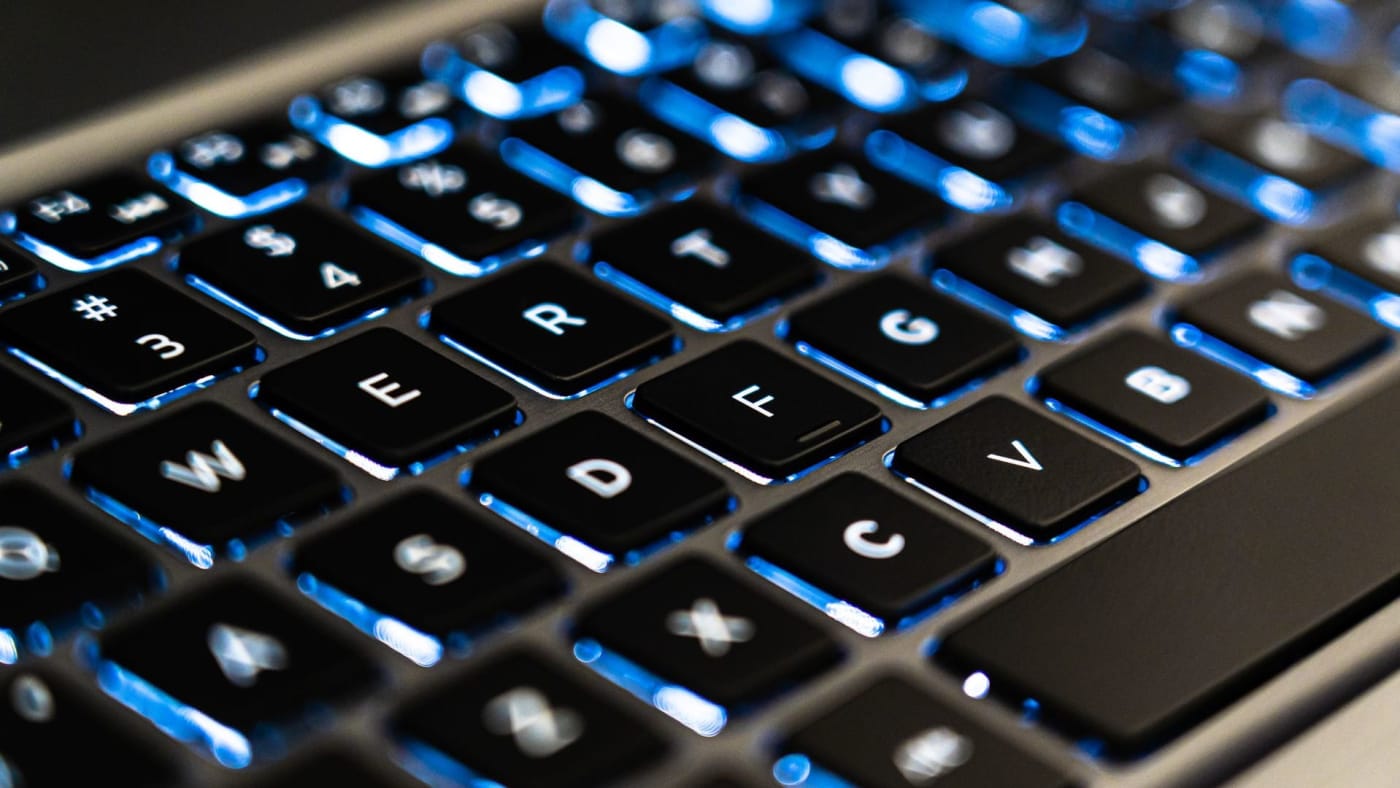 Close-up de teclado de computador com retroiluminação azul destacando as teclas pretas.