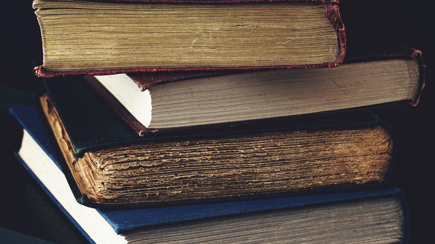 Pilha de livros antigos de capa dura sobre um fundo escuro.