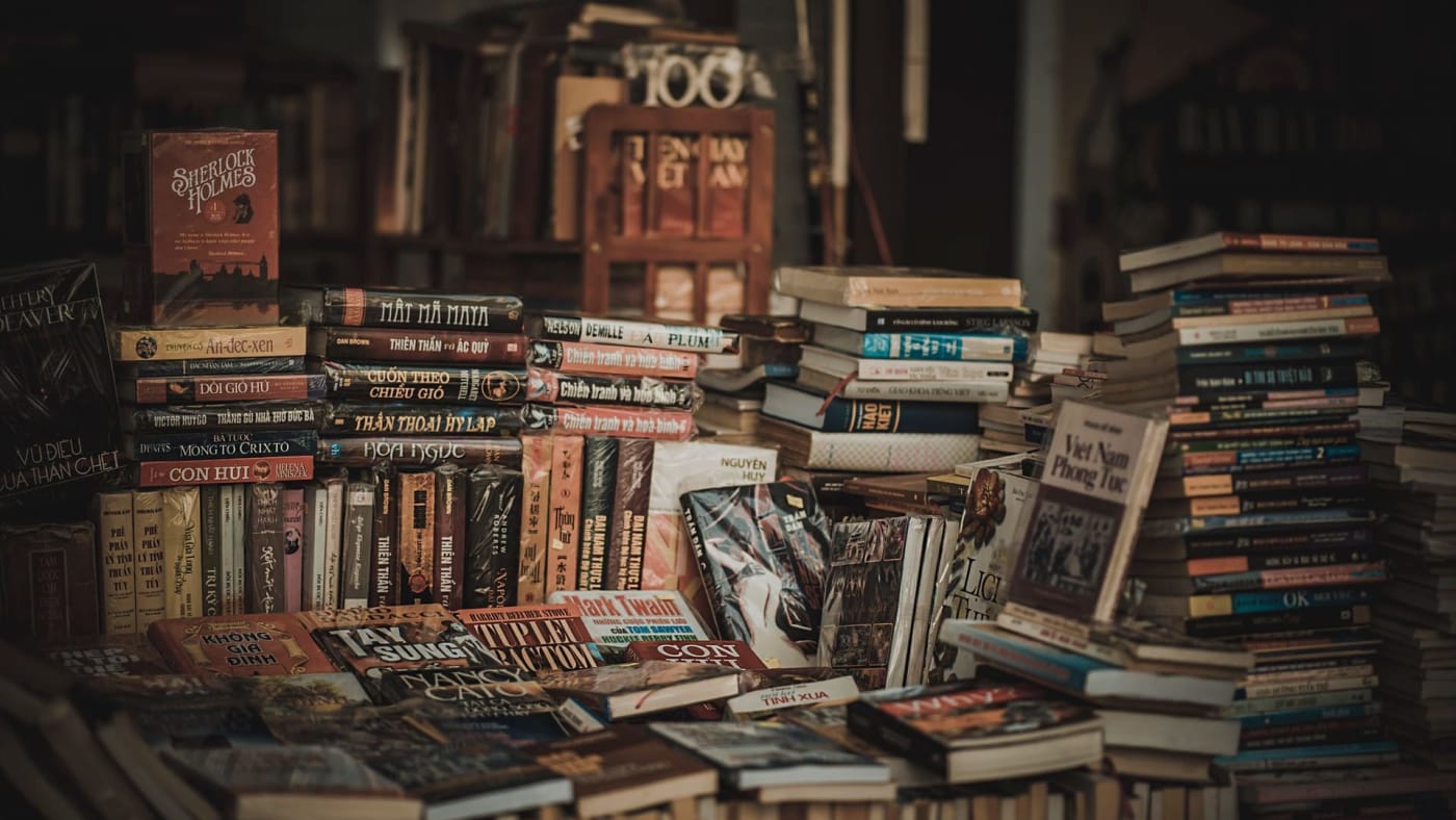 Pilhas e prateleiras repletas de livros diversos em um sebo ou livraria.