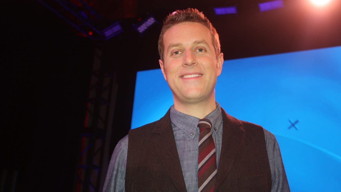 Geoff Keighley sorrindo em estúdio vestindo colete e gravata listrada