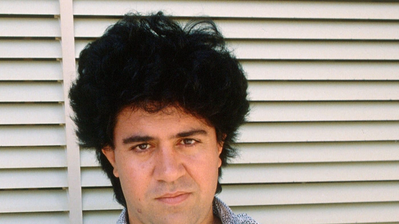 Pedro Almodóvar jovem olhando para a câmera em frente a uma persiana