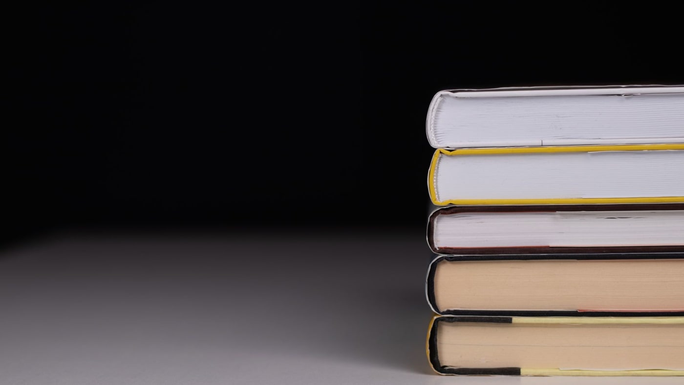 Pilha de livros fechados sobre uma superfície clara contra fundo escuro.