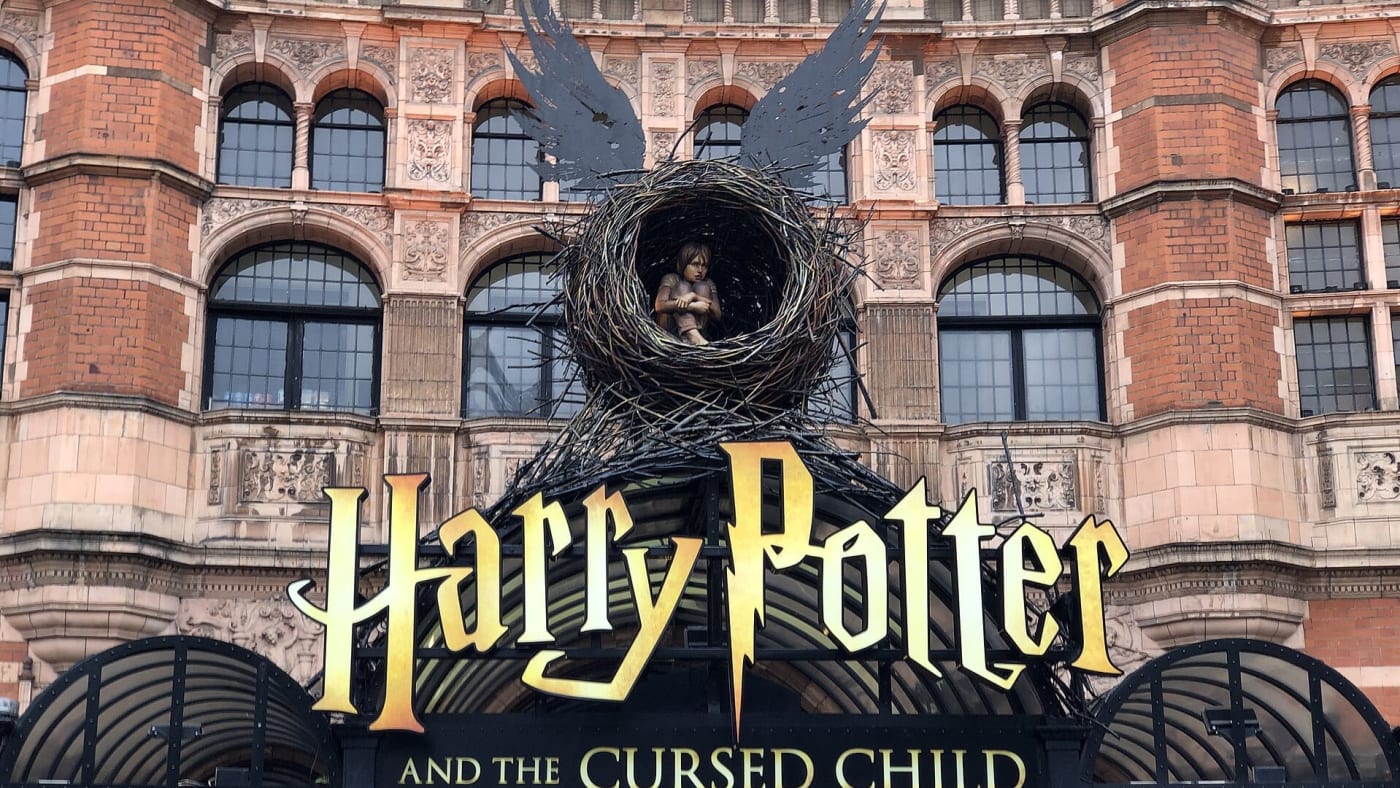 Fachada do teatro com letreiro dourado da peça Harry Potter and the Cursed Child sob escultura de um menino em um ninho alado.