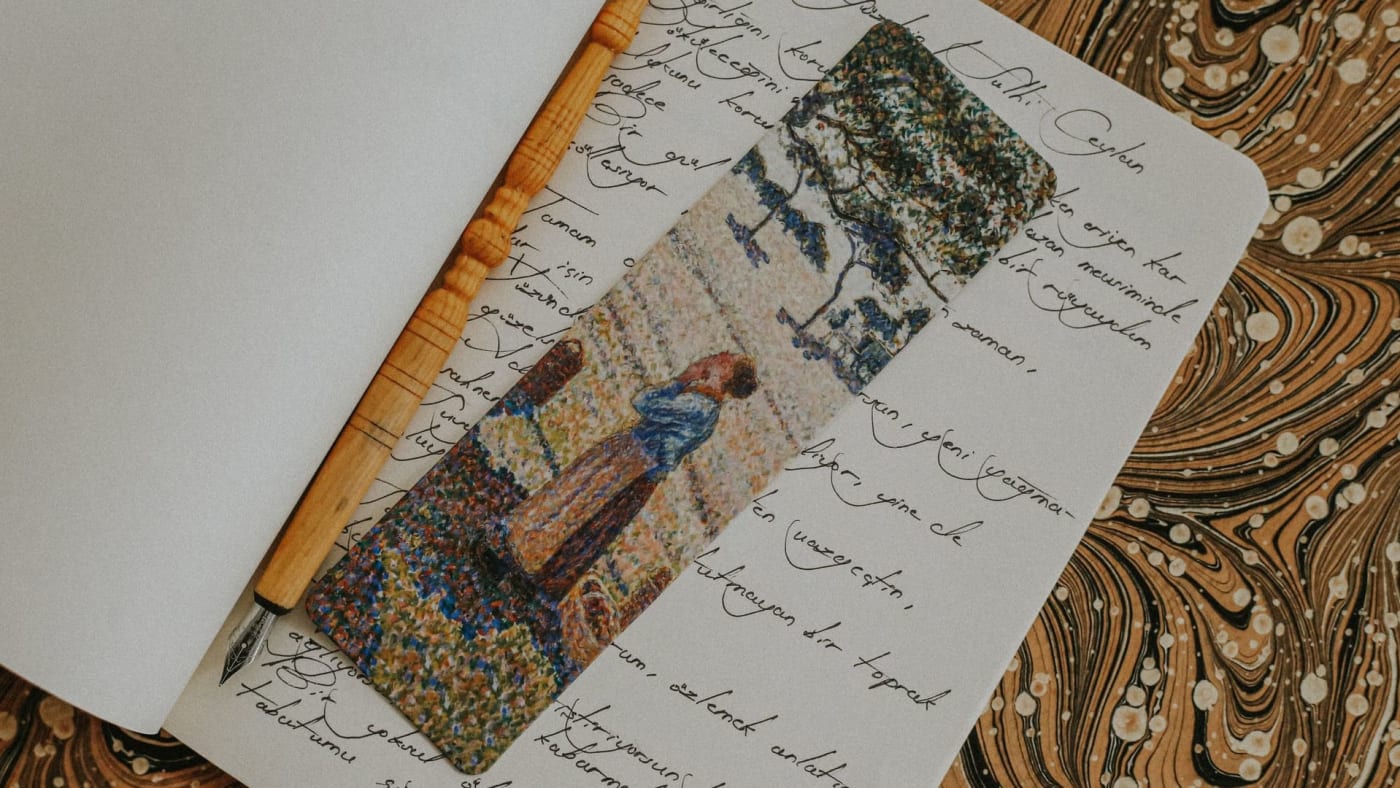 Caderno aberto com anotações manuscritas, caneta de ponta metálica e marcador de página artístico.