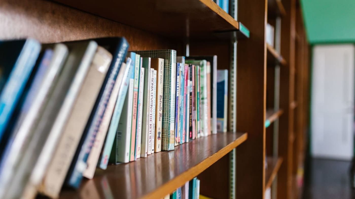 Livros perfilados em prateleiras de madeira dentro de uma biblioteca.