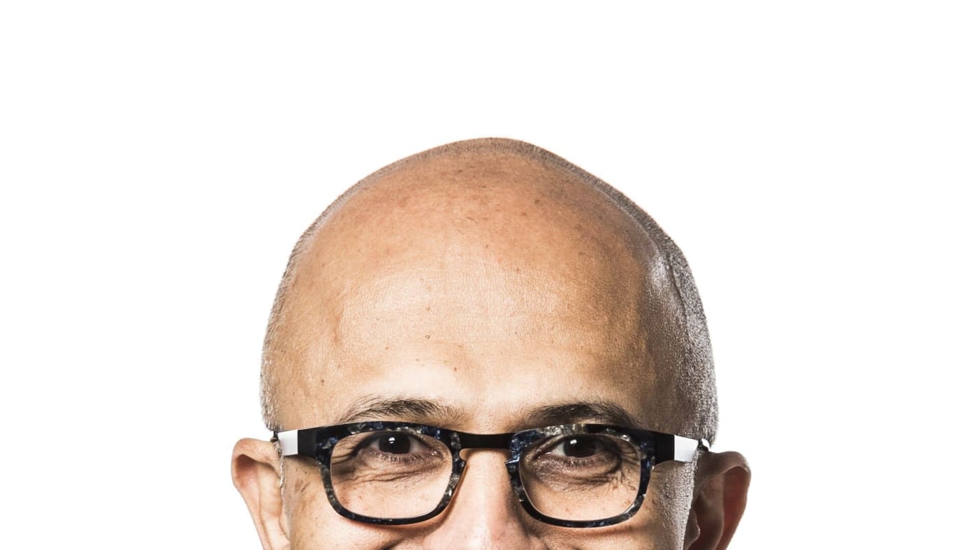 Retrato de Satya Nadella sorrindo com óculos e blazer azul