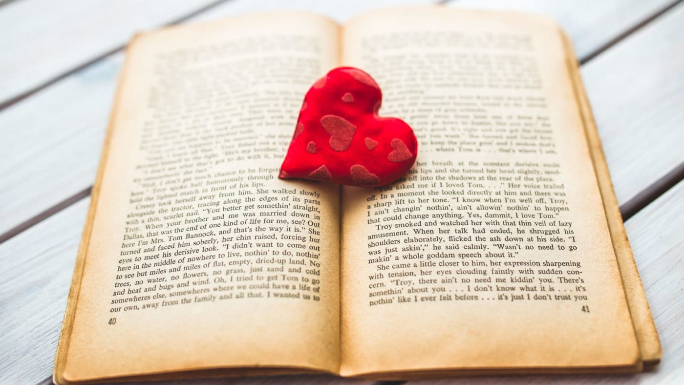 Livro aberto com um coração vermelho de tecido sobre as páginas.