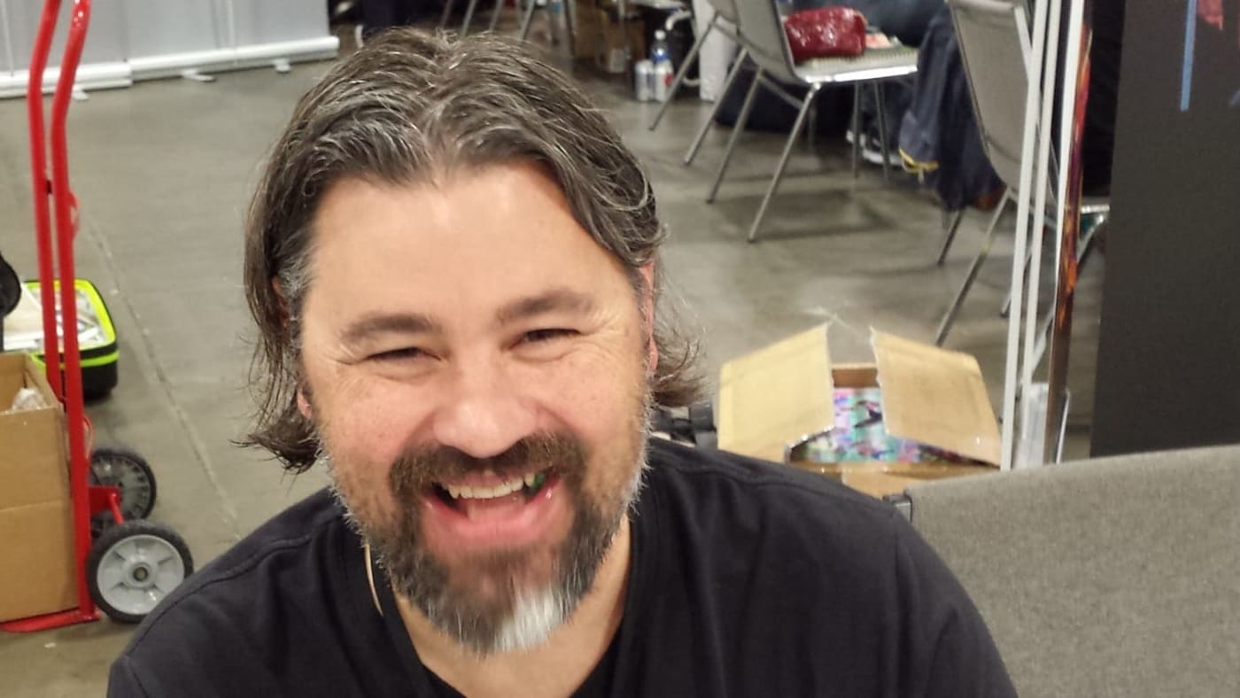 Jonathan Hickman sorri sentado a uma mesa durante um evento