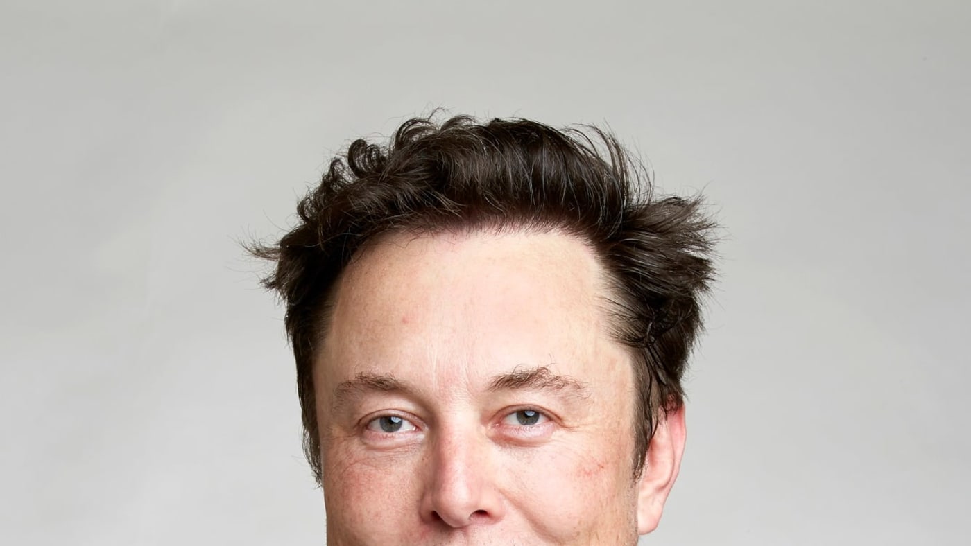 Elon Musk posa para foto vestindo paletó preto e camisa branca aberta