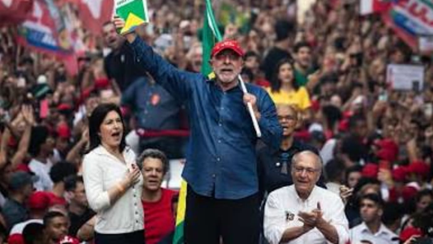 Lula, de boné vermelho, ergue um livro em cima de um carro de som na Avenida Paulista, cercado por apoiadores com bandeiras