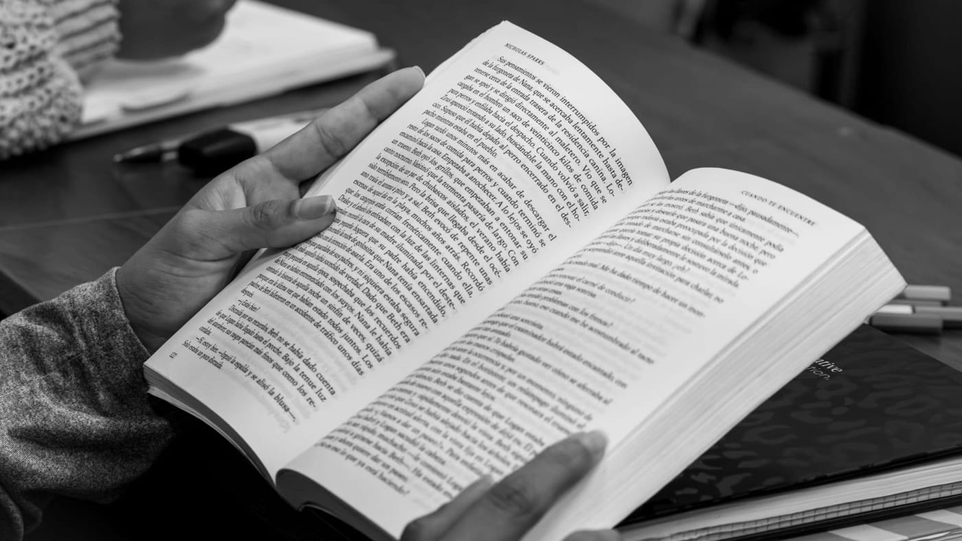 Mãos de uma pessoa segurando um livro aberto em preto e branco.