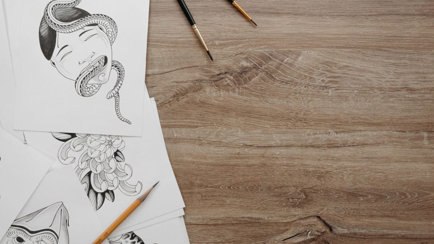Mesa de madeira com ilustrações em preto e branco no estilo japonês, pincéis e lápis