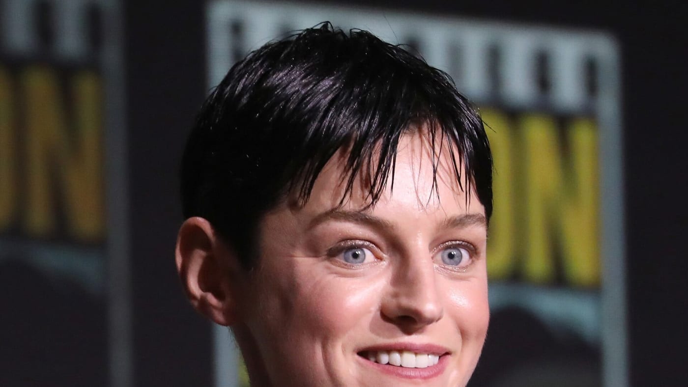 Emma Corrin sorri em frente a um microfone durante evento