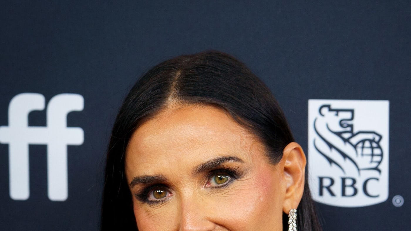 Demi Moore sorri em evento vestindo camisa branca e gravata preta.