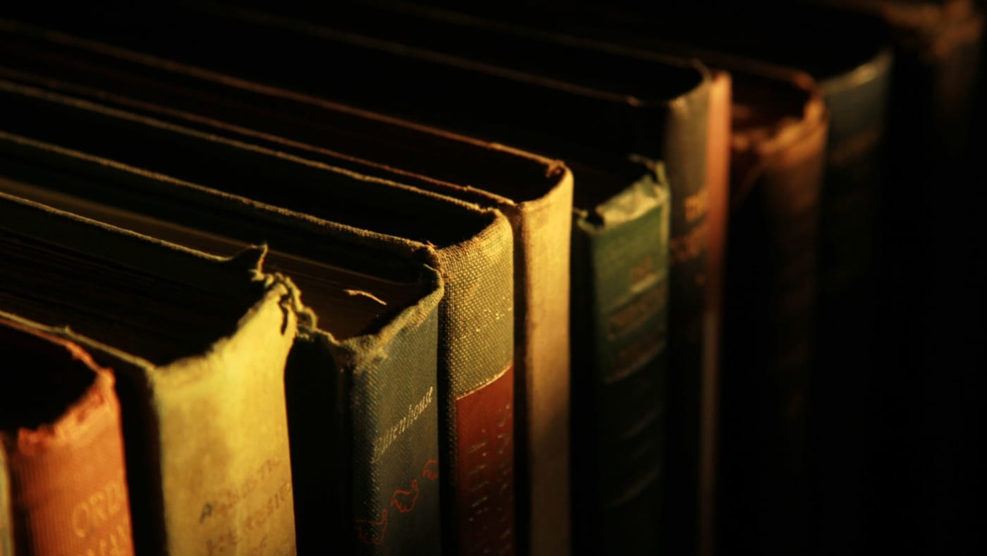 Fileira de livros antigos com lombadas gastas sob luz quente