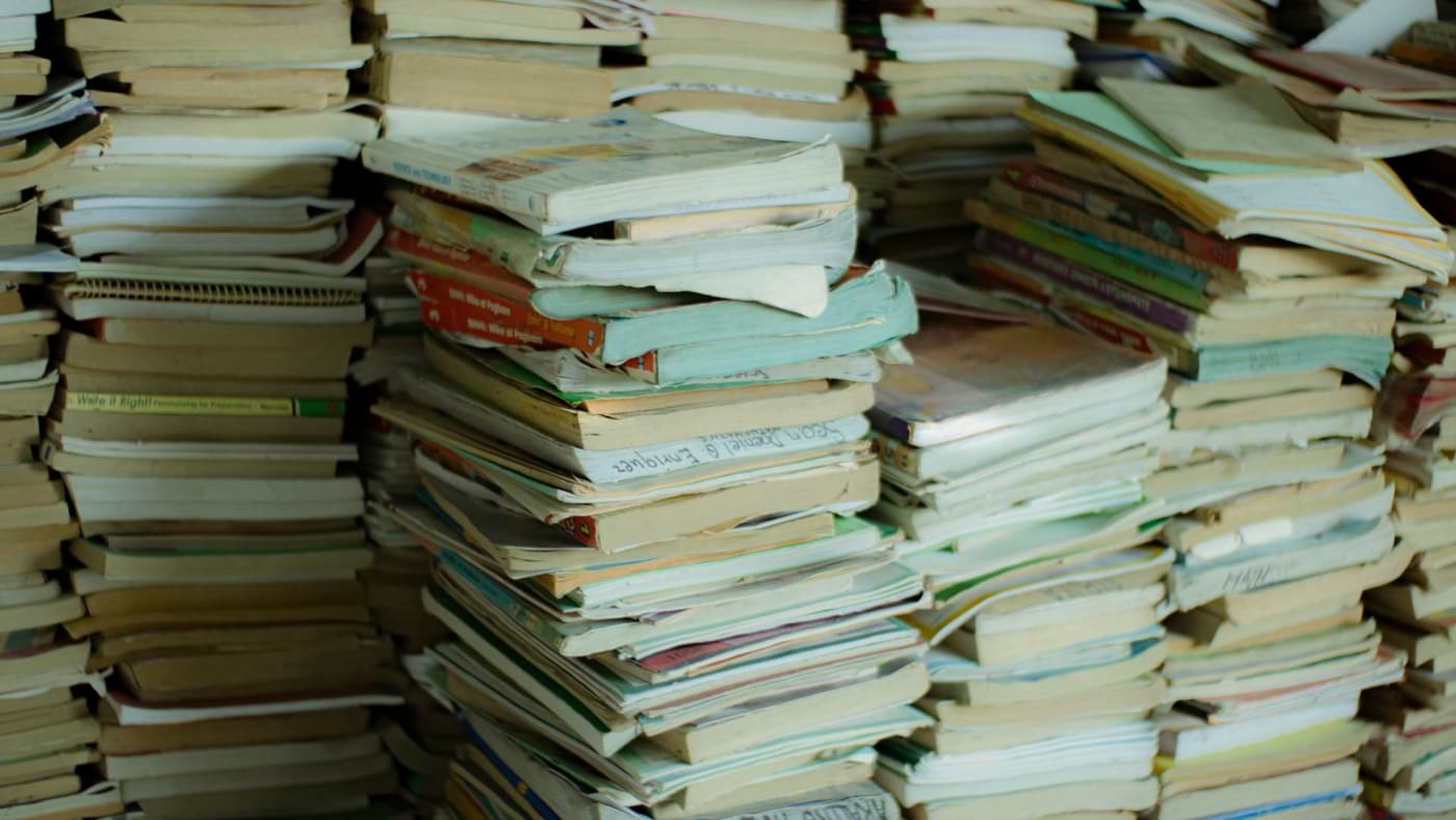 Pilhas volumosas de livros e cadernos usados e desgastados empilhados.