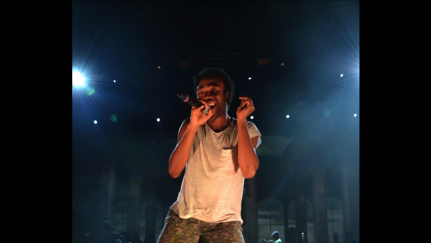 Donald Glover canta com microfone no palco durante apresentação musical