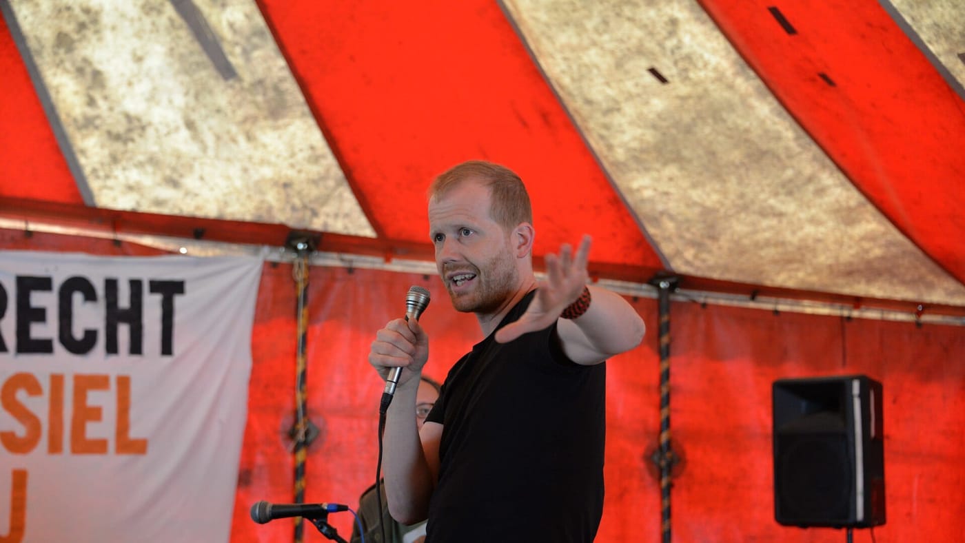 Andreas Malm segura um microfone e gesticula enquanto discursa em um evento.