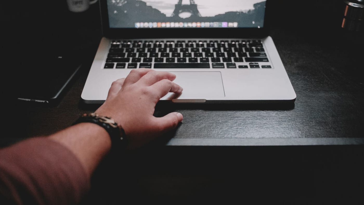 Mão de uma pessoa apoiada no touchpad de um notebook aberto em ambiente escuro.