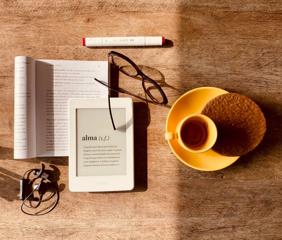 Leitor de e-book apoiado sobre uma mesa ao lado de uma xícara