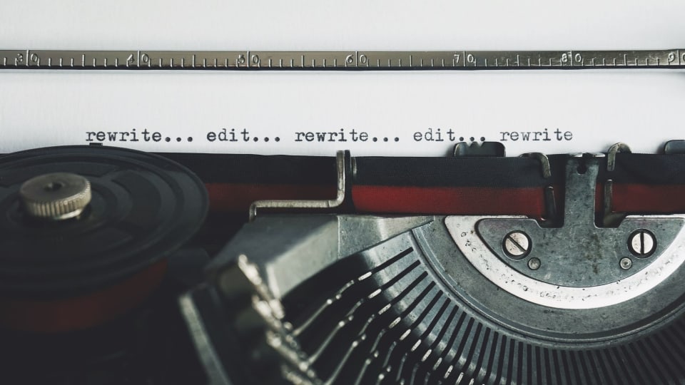Folha numa máquina de escrever antiga com as palavras rewrite e edit datilografadas em sequência.