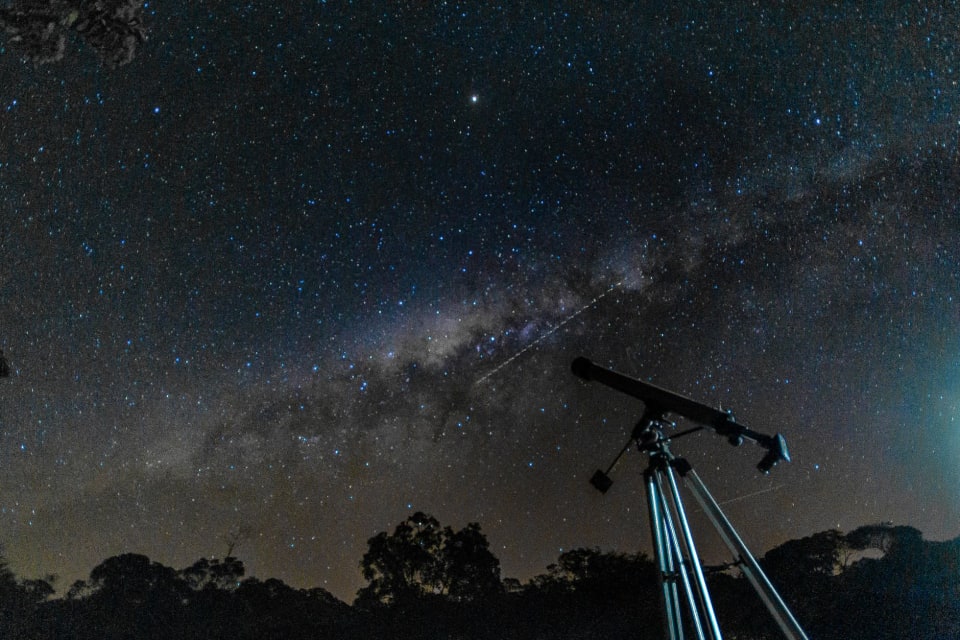 Telescópio apontado para um céu noturno cheio de estrelas.