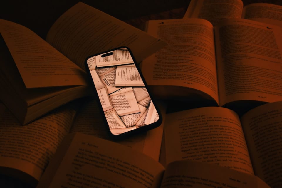 Celular com páginas de livro na tela, deitado sobre vários livros abertos.