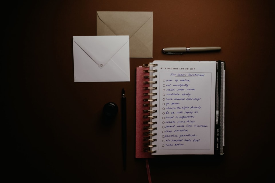 Caderno aberto com listas de palavras escritas à mão e uma caneta ao lado.