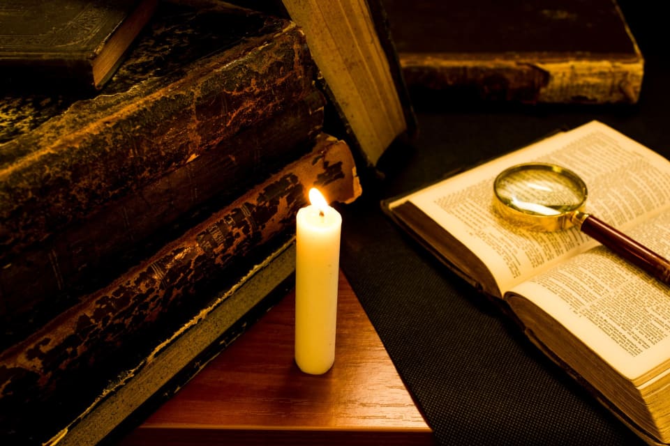 Livro antigo aberto sobre uma mesa, iluminado por uma vela.