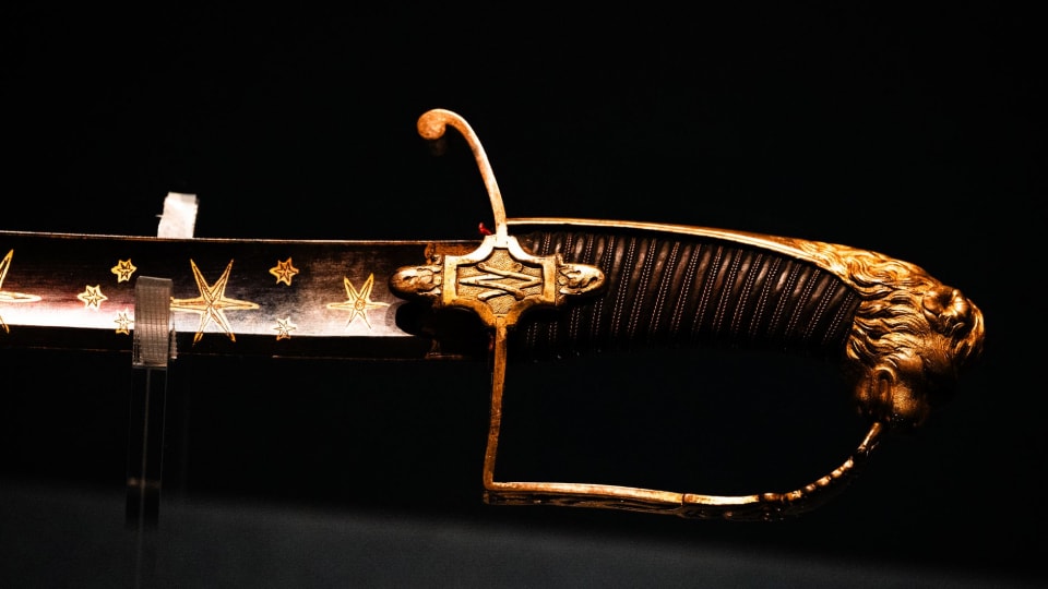 Espada antiga de lâmina longa exposta num museu, vista de perto.