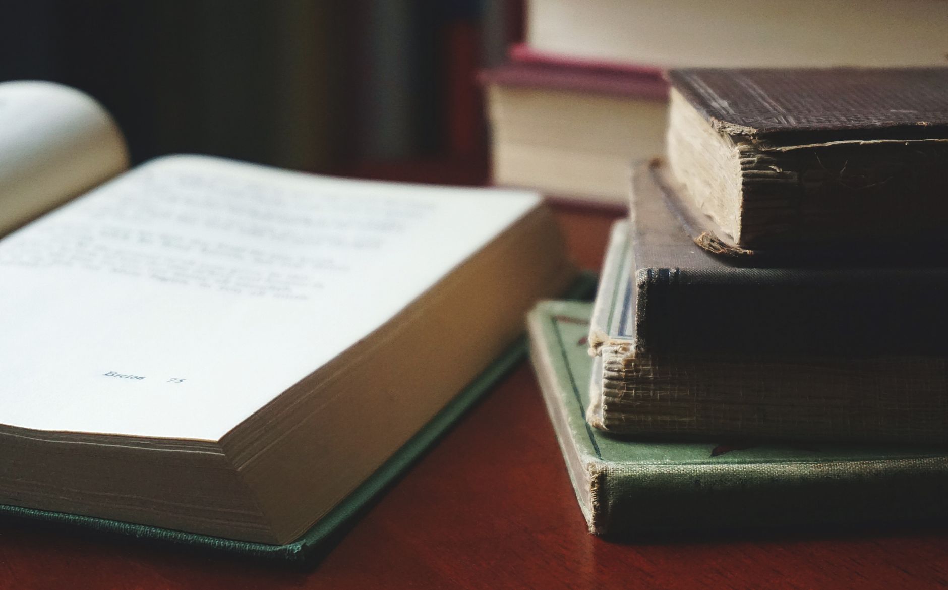 Livro aberto sobre uma mesa, ao lado de uma pilha de livros de capas e formatos diferentes