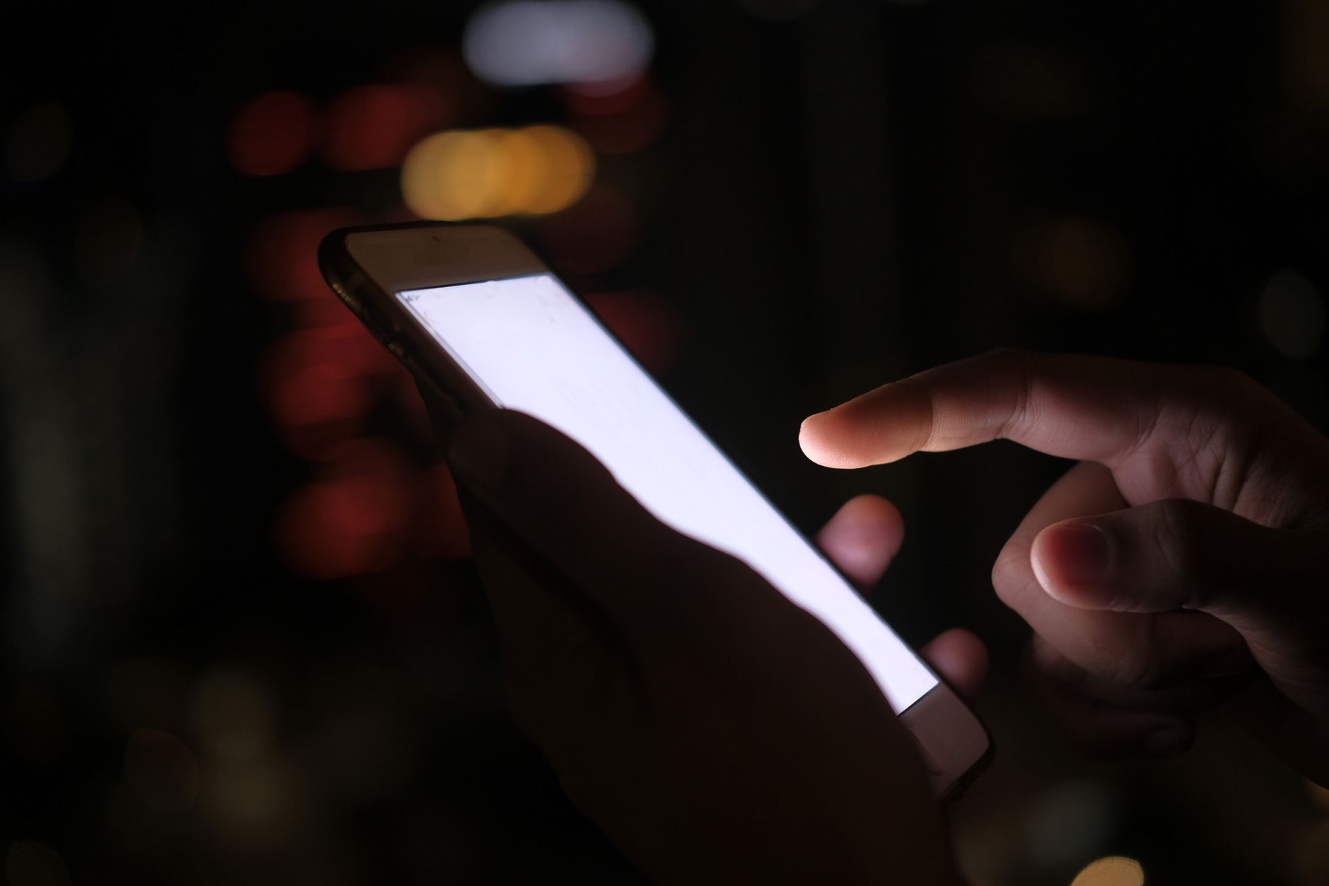 mãos segurando um celular aceso no escuro, tela cheia de texto