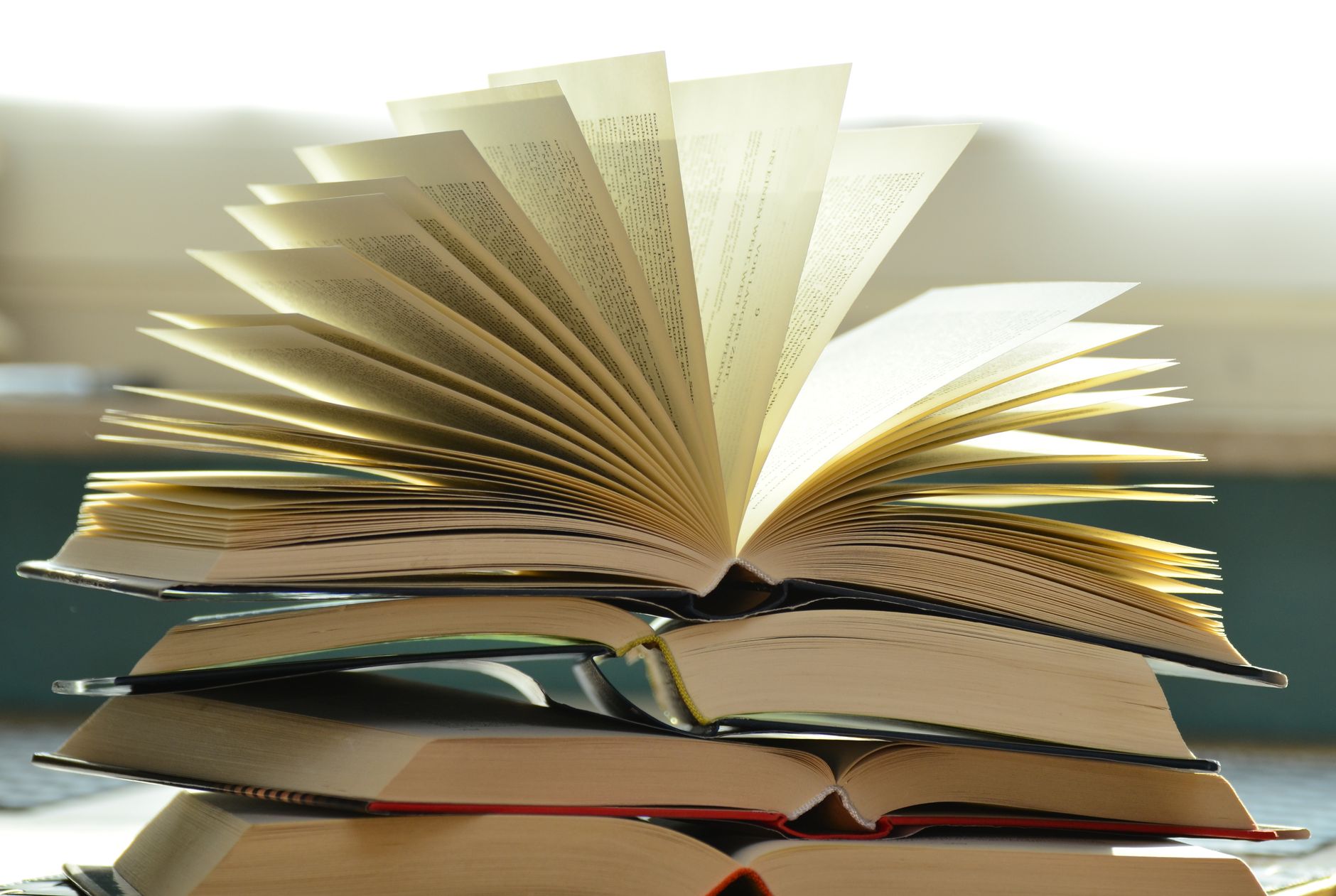 Livro aberto com as folhas em leque, apoiado sobre uma pilha de outros livros.