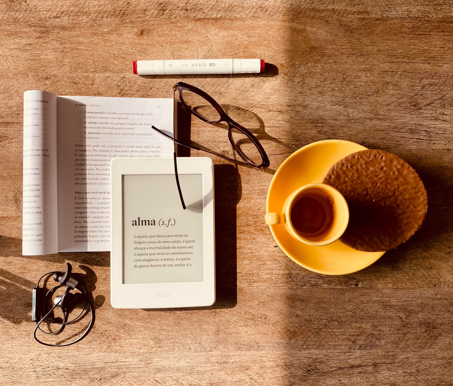 Um leitor de e-book com texto na tela ao lado de um livro impresso aberto sobre uma mesa