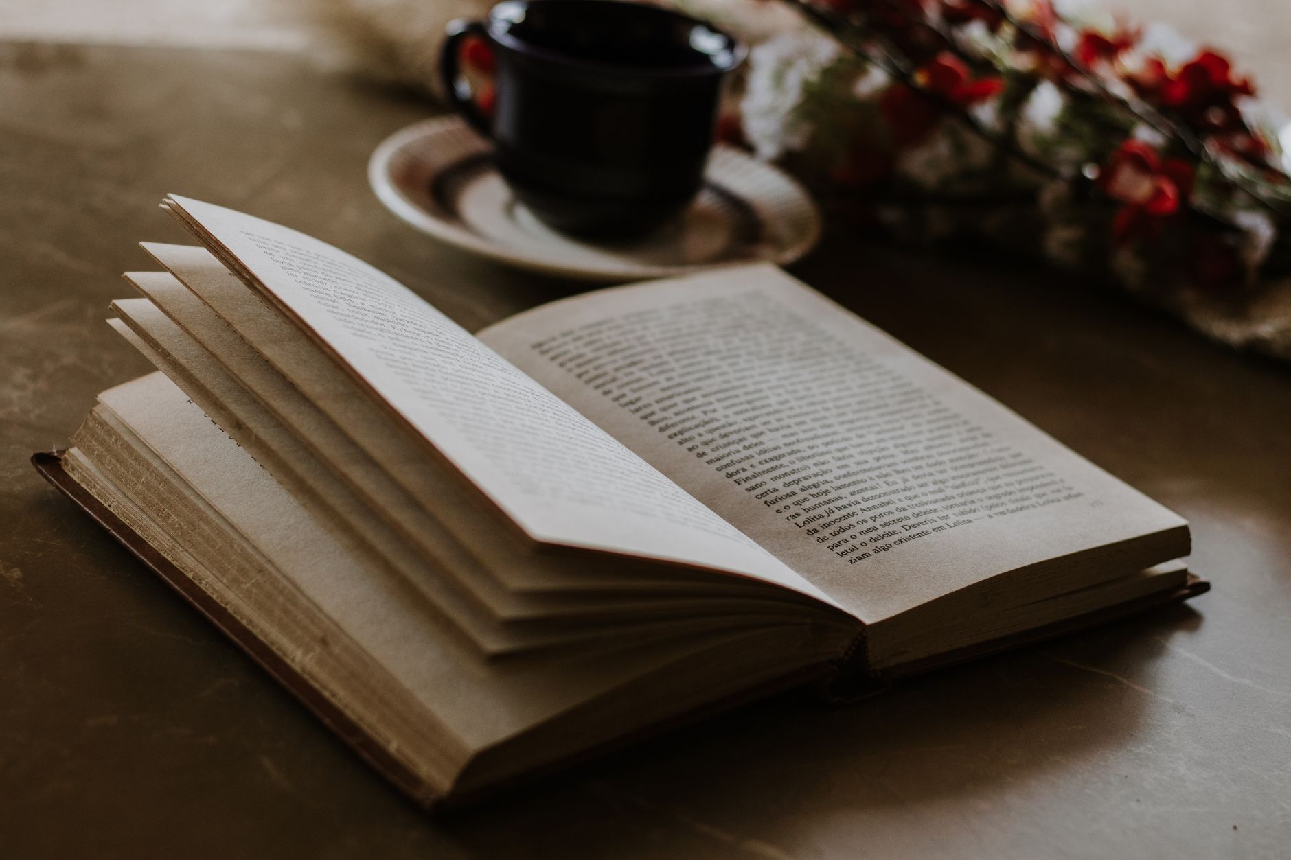 Livro aberto sobre uma mesa ao lado de uma xícara, sob luz lateral quente