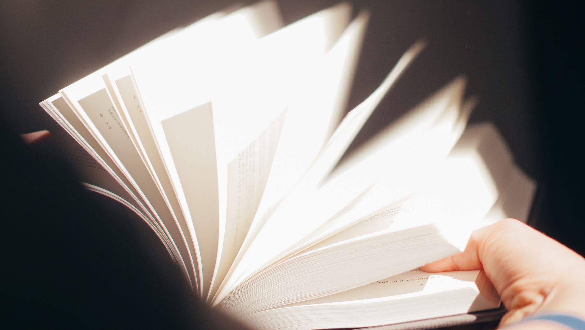Primeiras páginas de um livro sendo viradas, sobre uma mesa