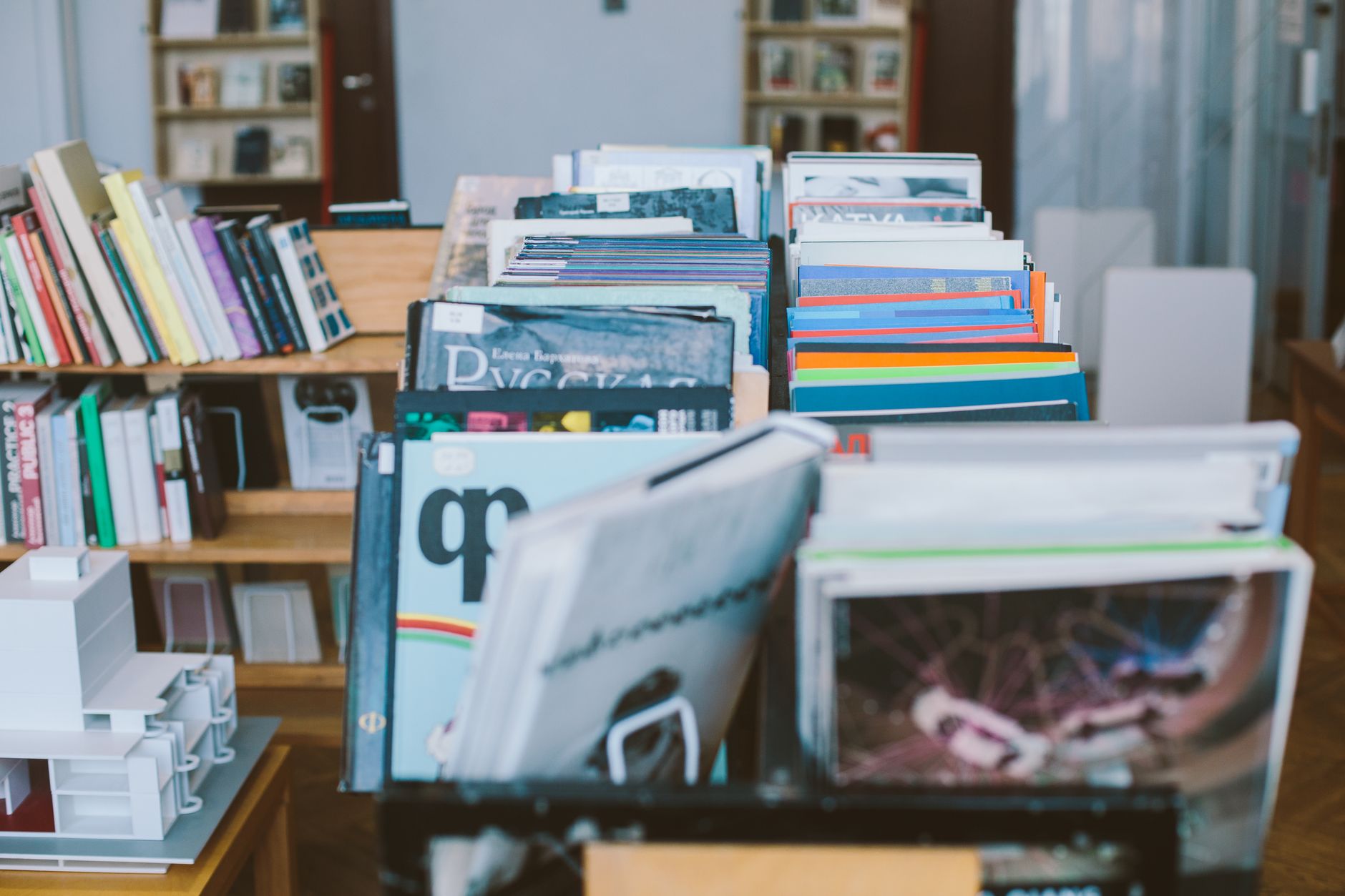 Expositor de livraria com revistas em pé em caixas e estantes de livros ao fundo.