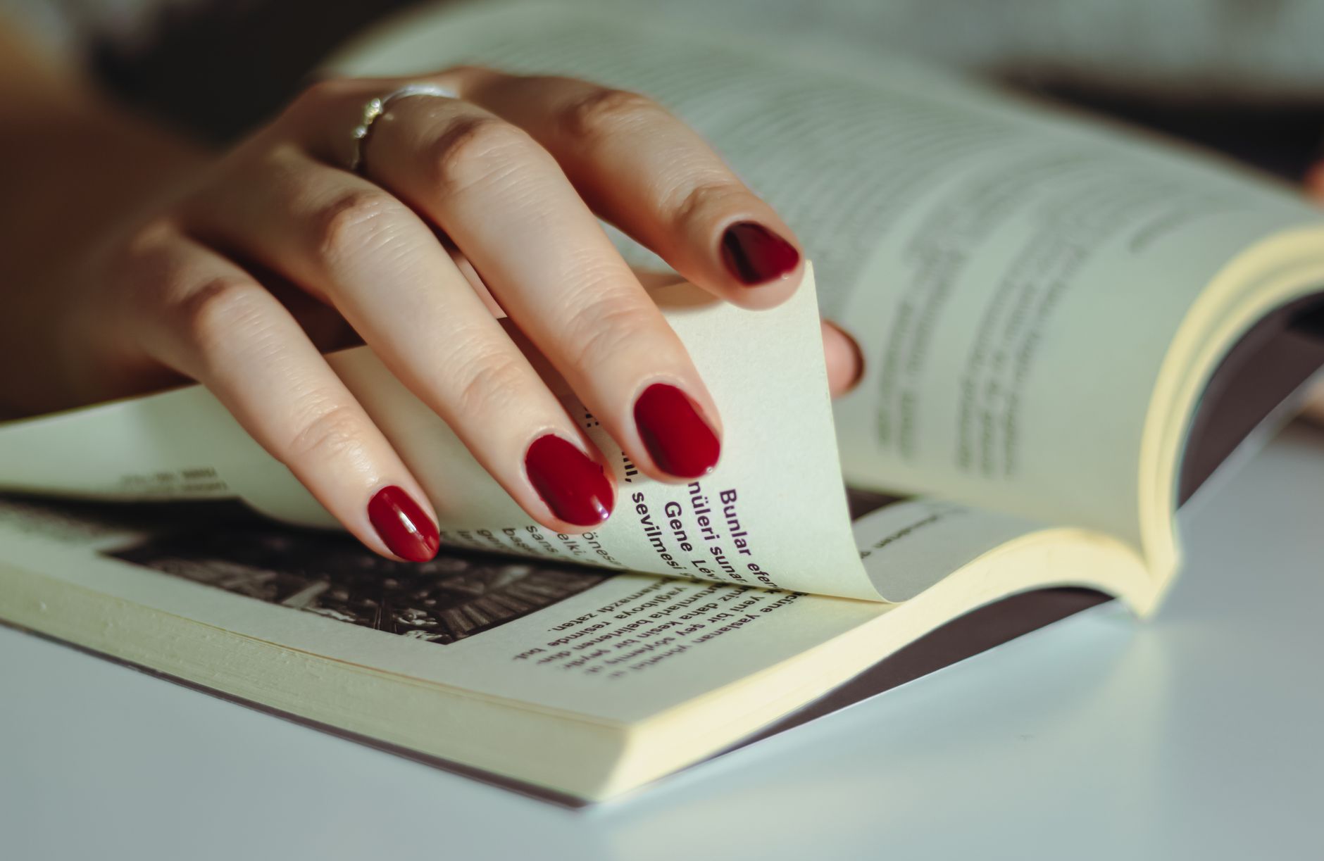 Mão virando a página de um livro aberto sobre uma mesa